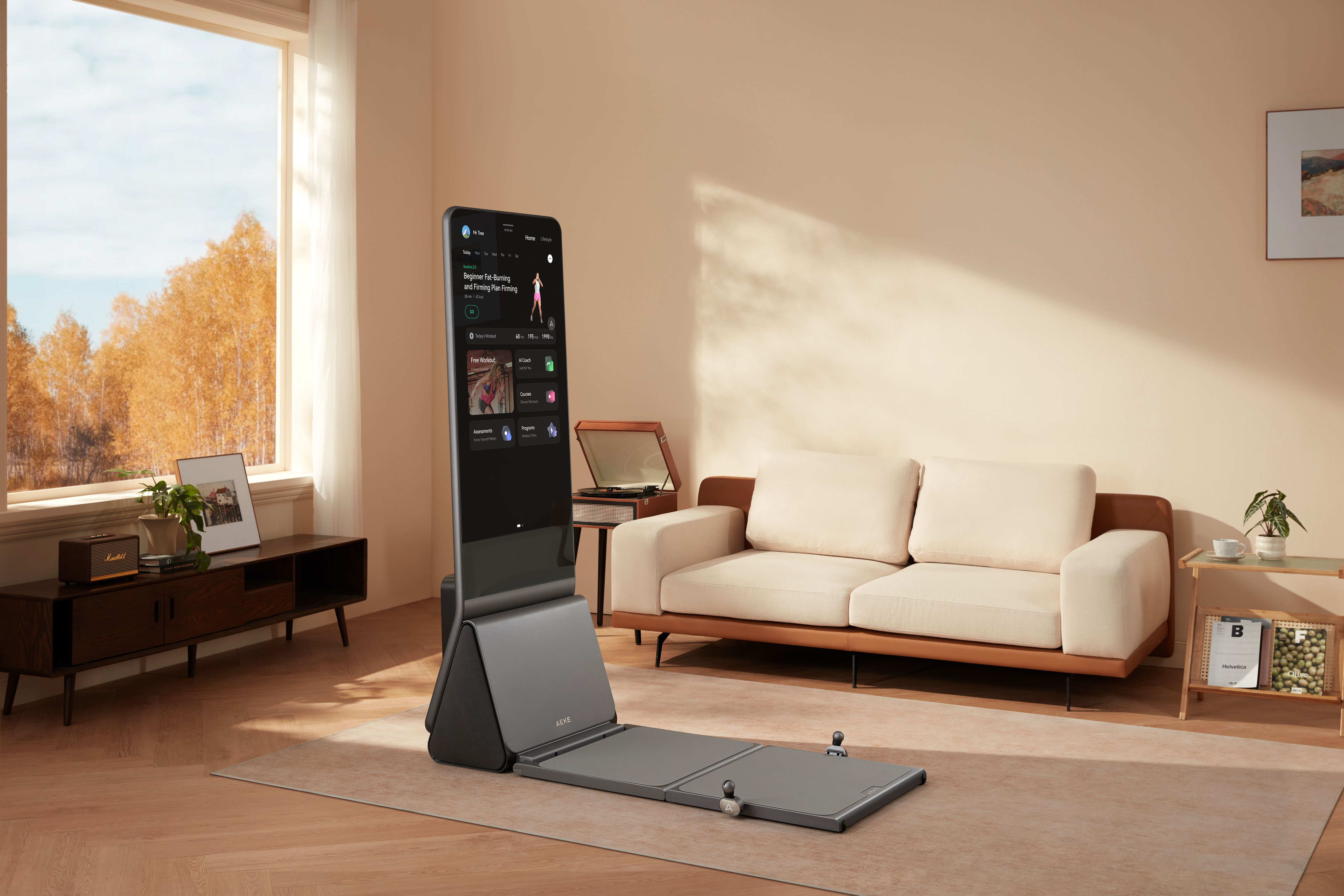 Freestanding touchscreen fitness system on a floor mat in front of a sofa, with its broad platform extending into the living room.