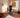 Two people interact with a connected home gym; one holds small hand controls while the other reaches toward its workout screen.