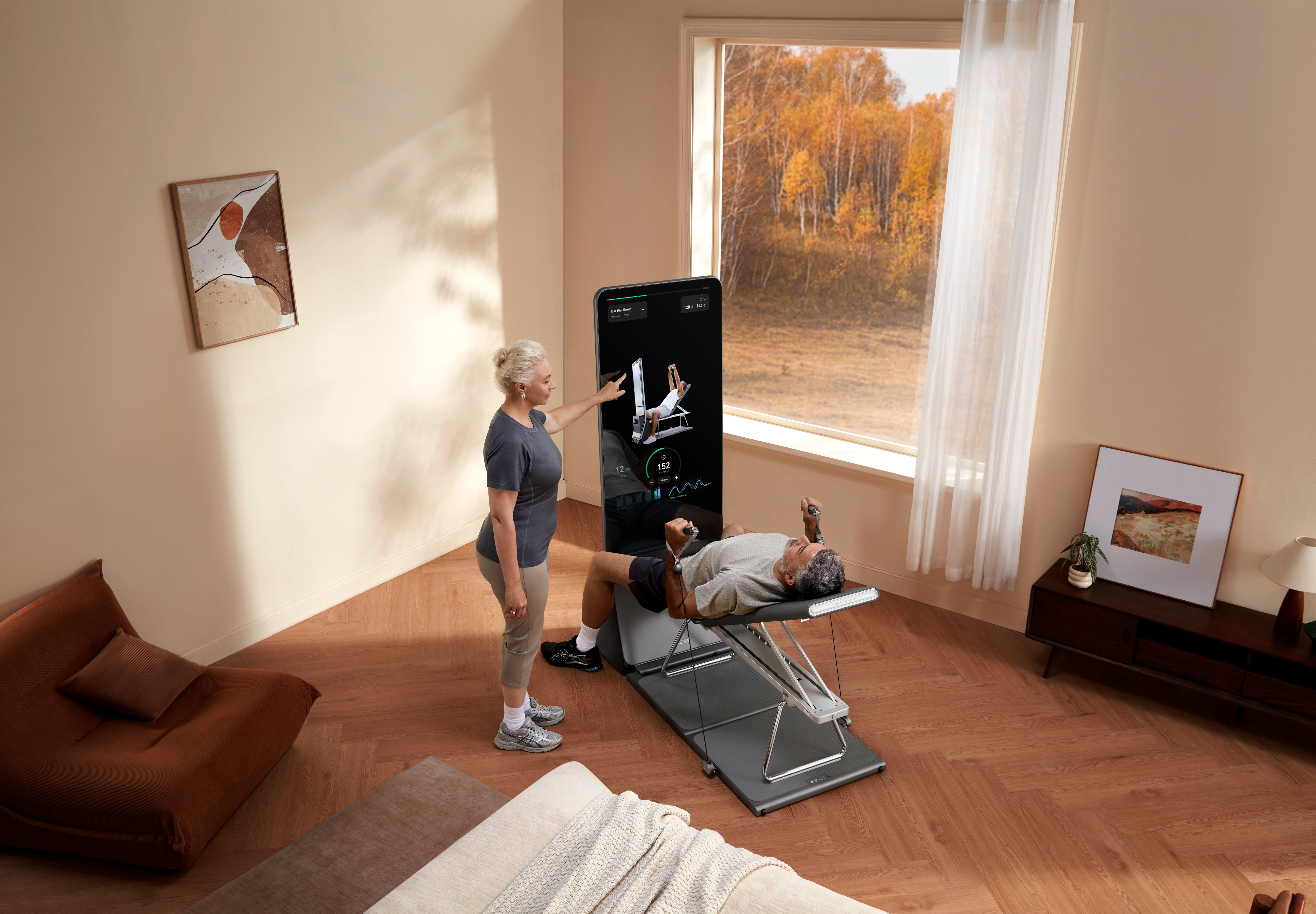A man uses a connected home gym on an adjustable bench while a woman reaches toward its touchscreen.