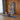A woman follows a trainer on a tall fitness display while holding a stretch at home.