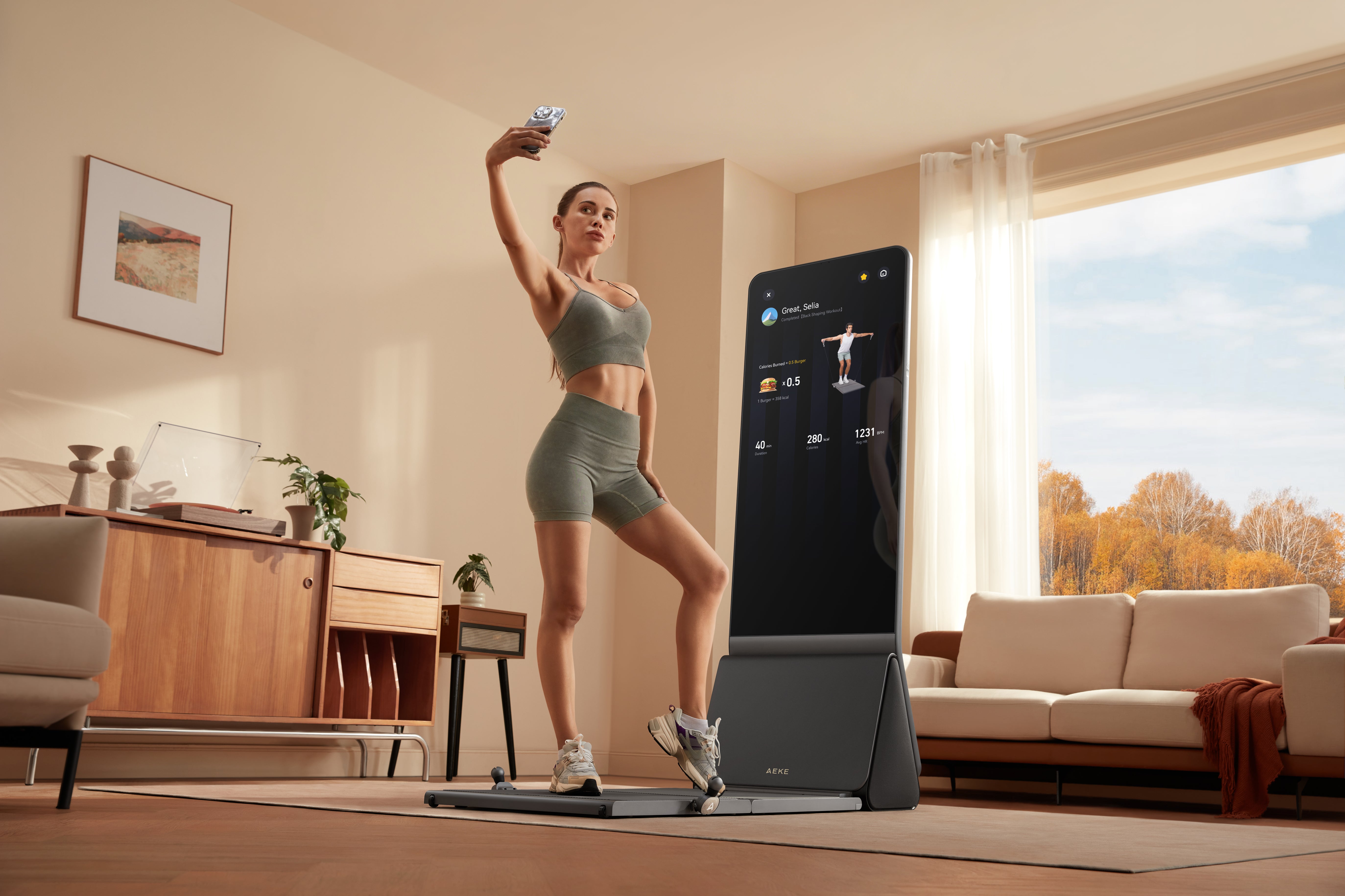 A woman in athletic wear taking a selfie while posing next to a smart mirror fitness device during a home workout session.