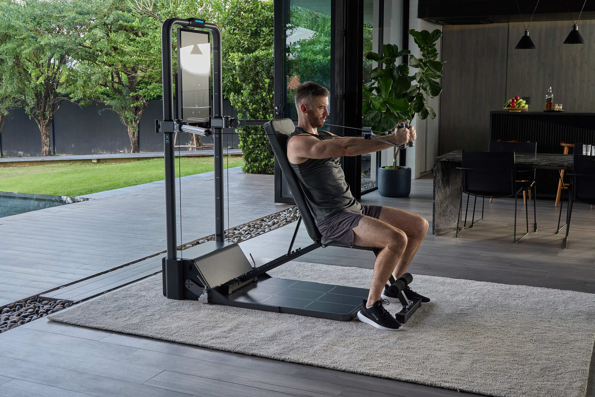 Man performing a seated cable row on a home strength-training machine in a modern room.