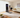 Woman using a compact home gym machine for a bent-over barbell exercise in a bright living room.